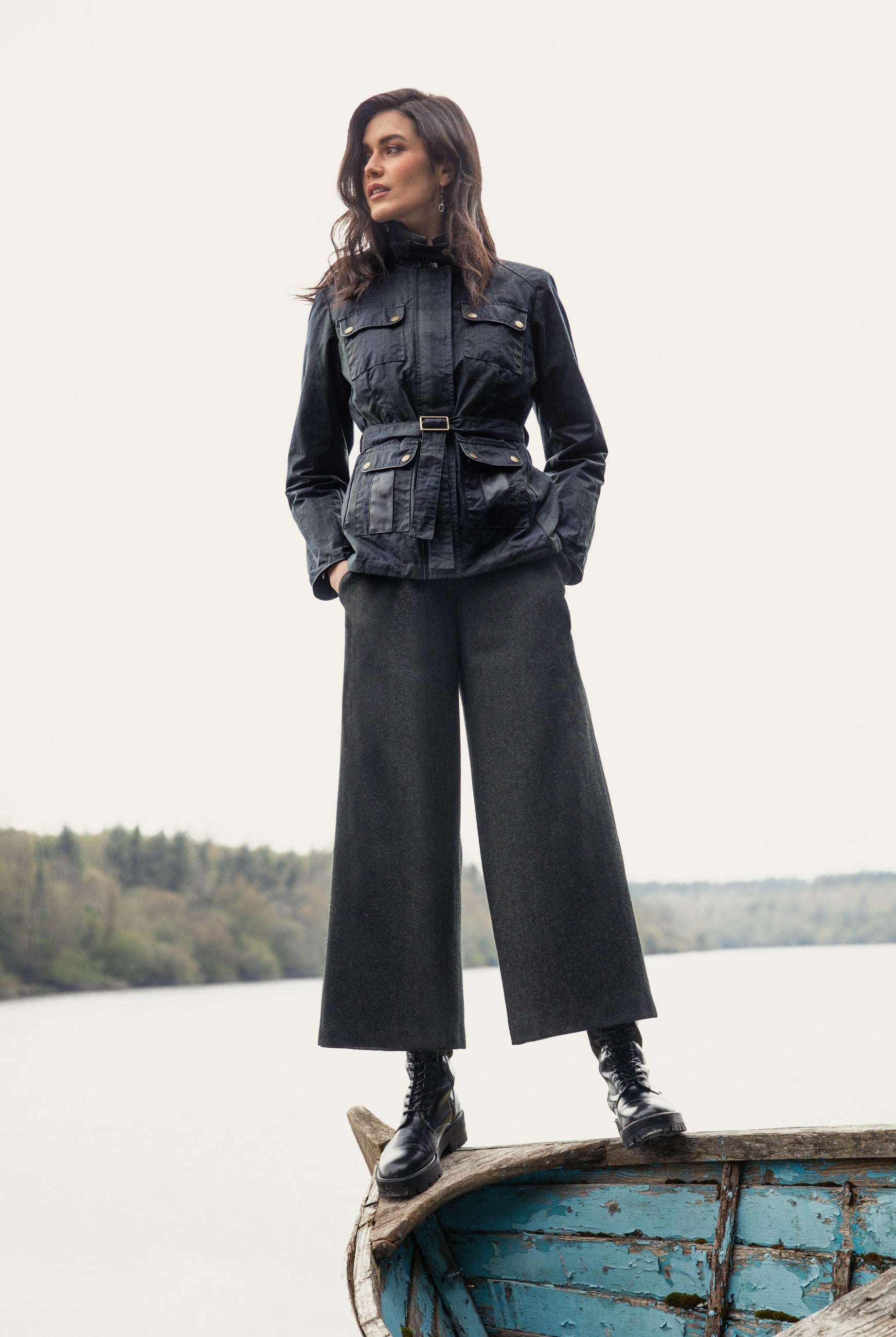 Girls standing on boat in Enya Green Tweed trousers and. black watch Cara wax jacket.
