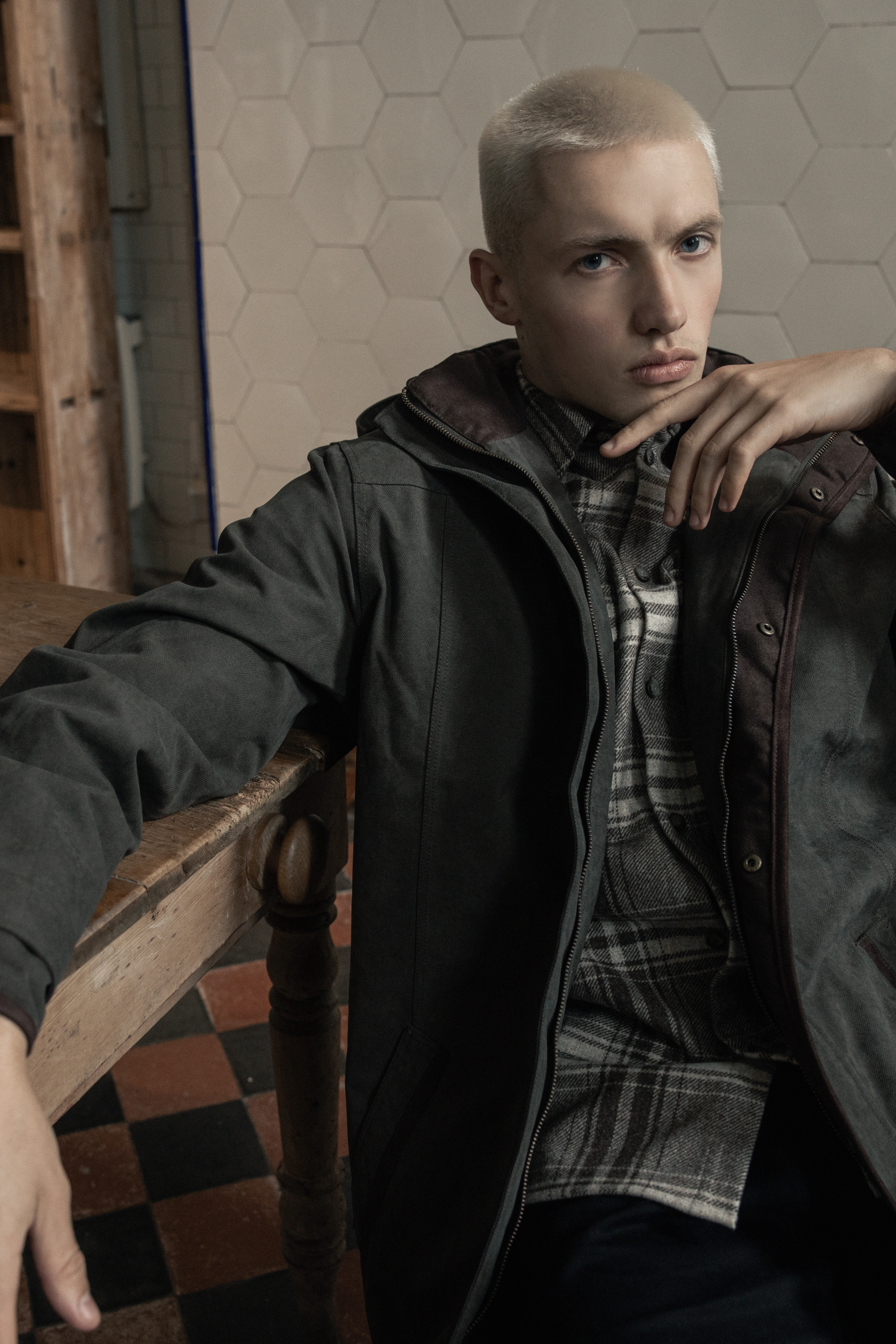 Man in basement kitchen leaning on table with Emmett waterproof coat in olive on