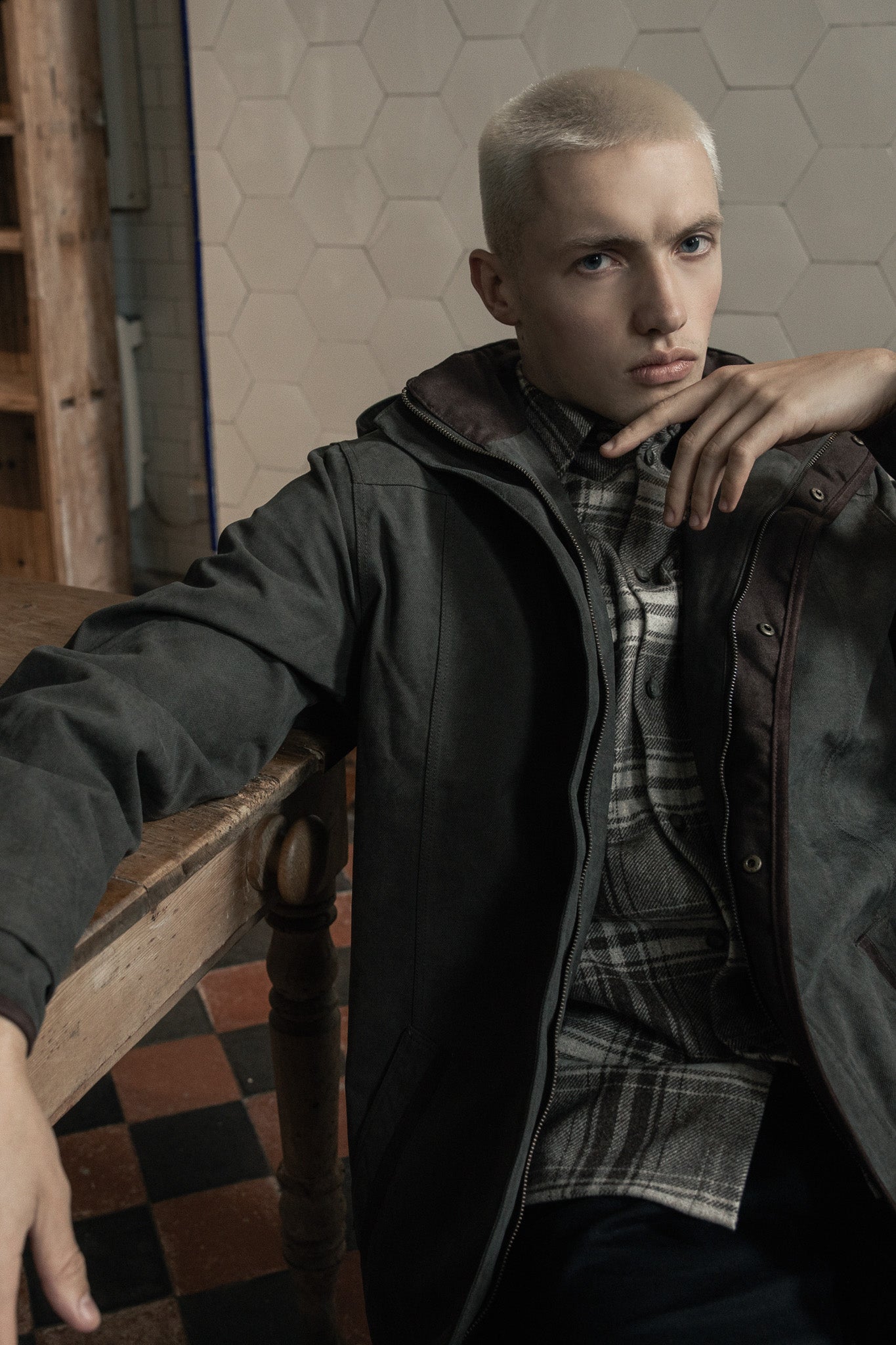 Man in basement kitchen leaning on table with Emmett waterproof coat in olive on