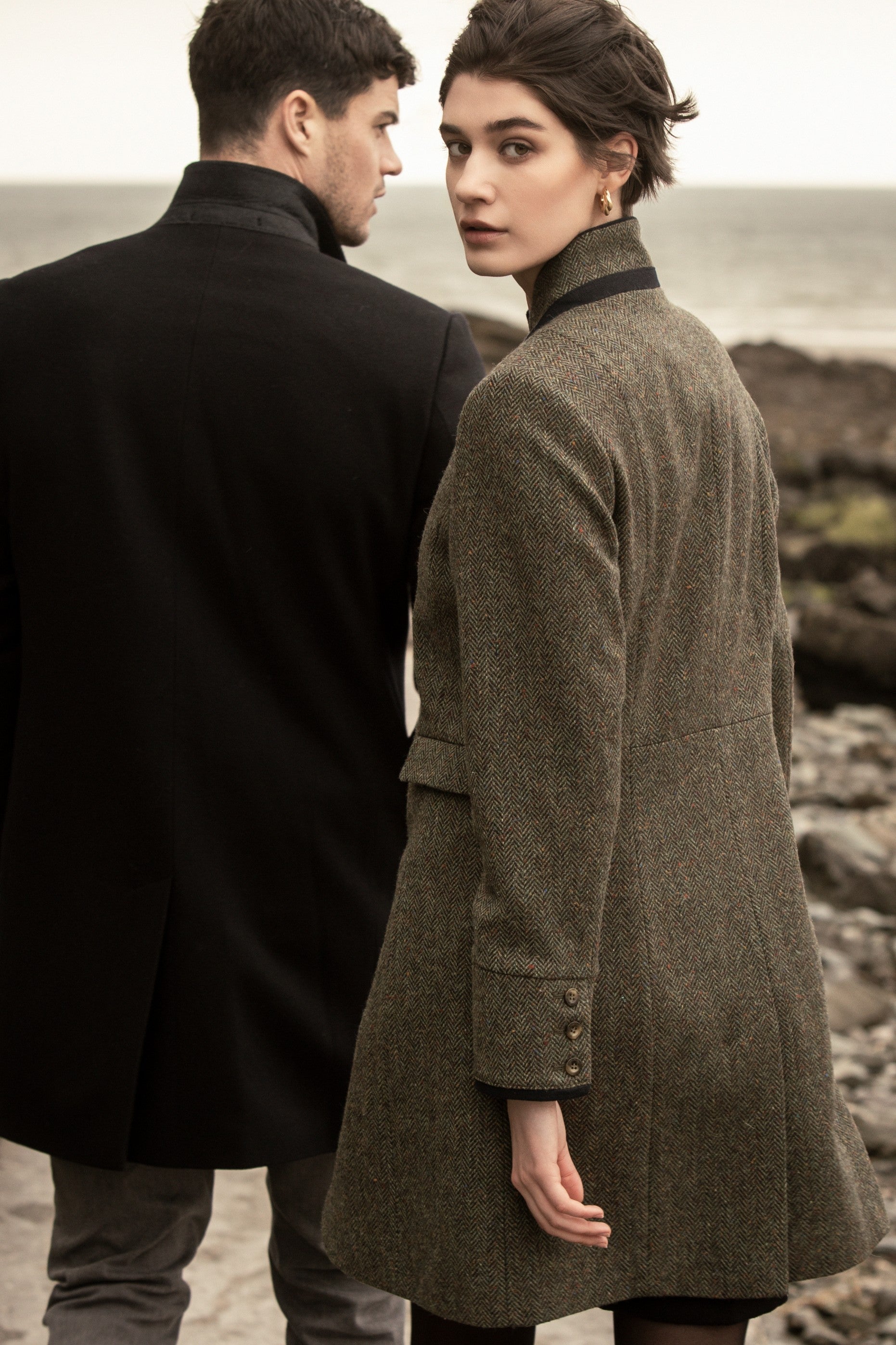 Man and woman walking on beach in long tweed coats.