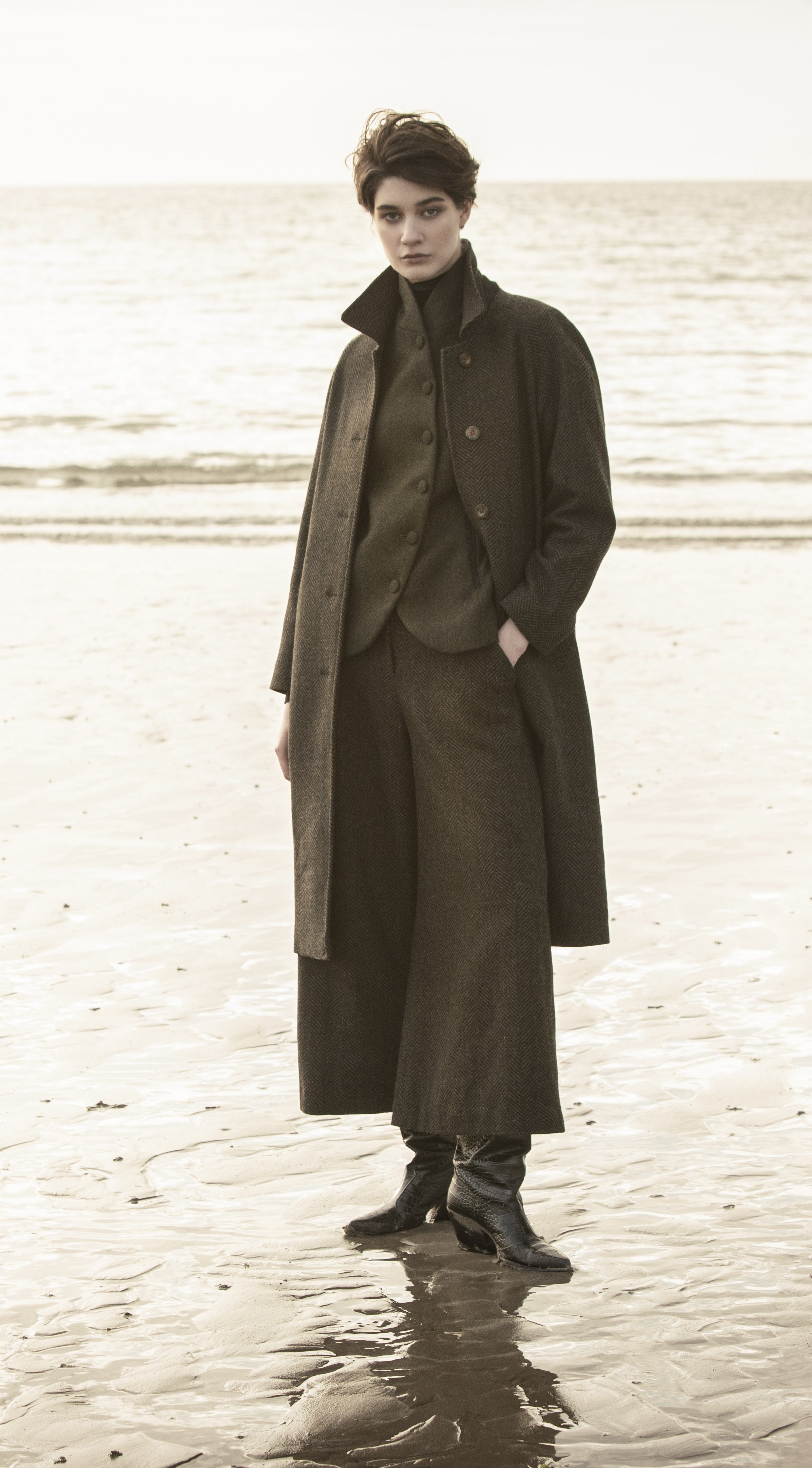 Woman on beach in tweed long jacket tweed jacket and Tweed pants.