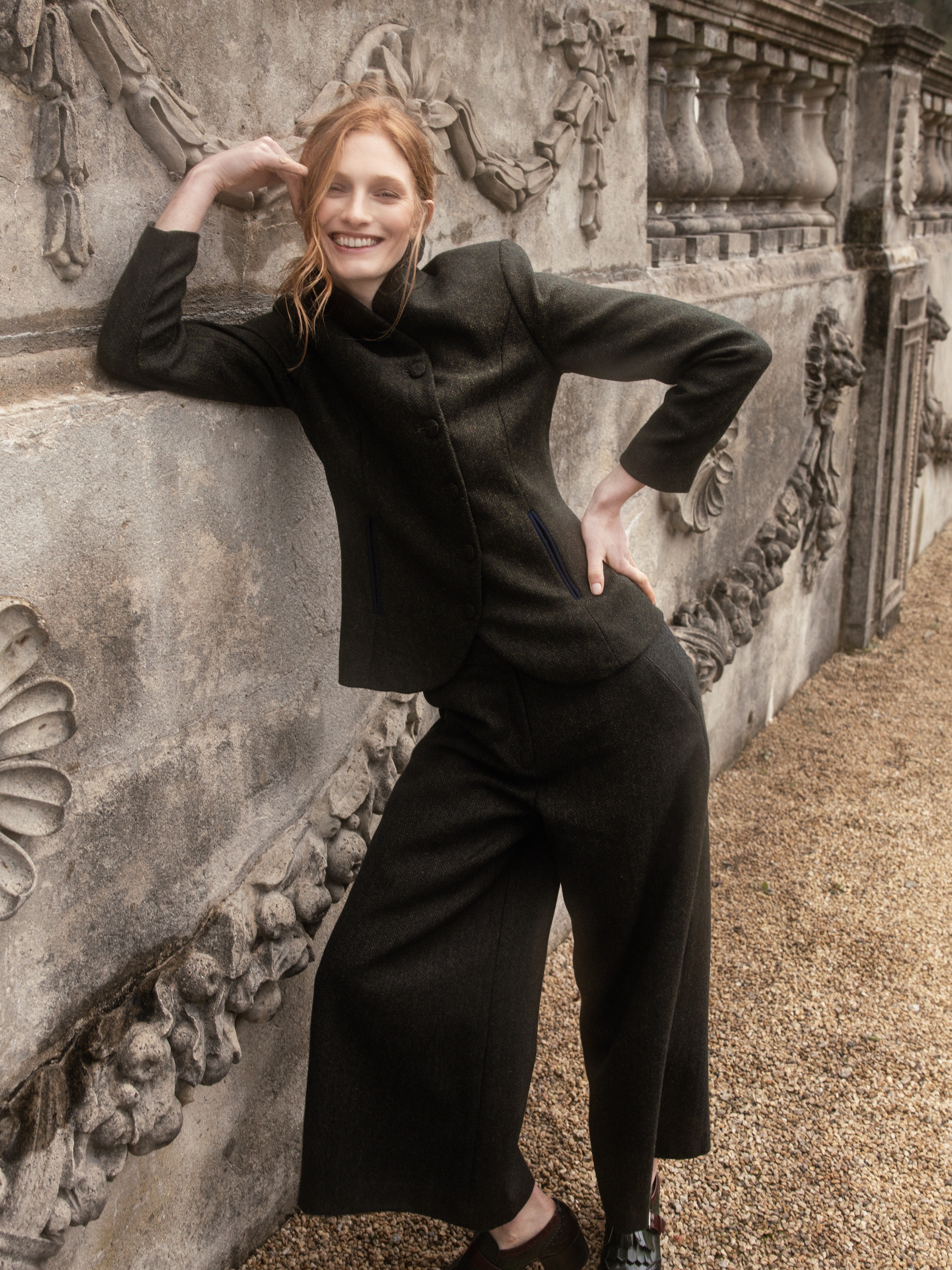Ginger girls leaning against ornate stonewall in a woman's three piece suit