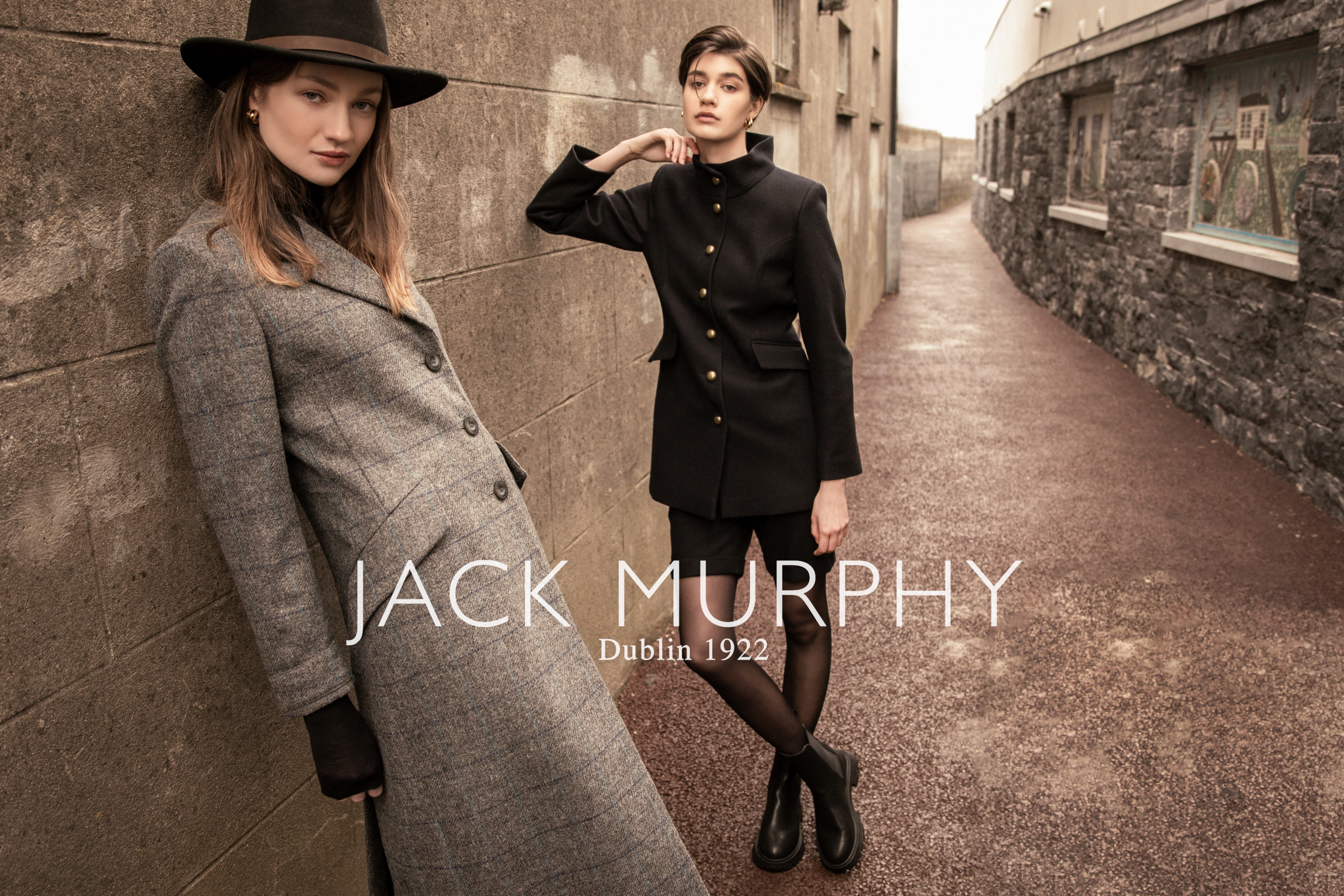 Two women leaning against Wall and tweed jackets and Boston felt hats.