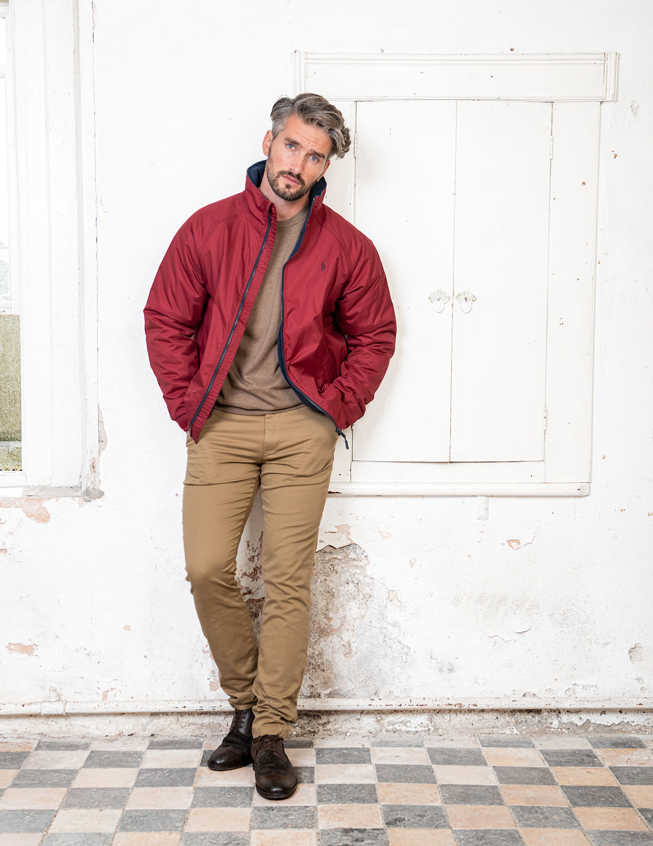 Man in waterproof red jackets leaning against wall.