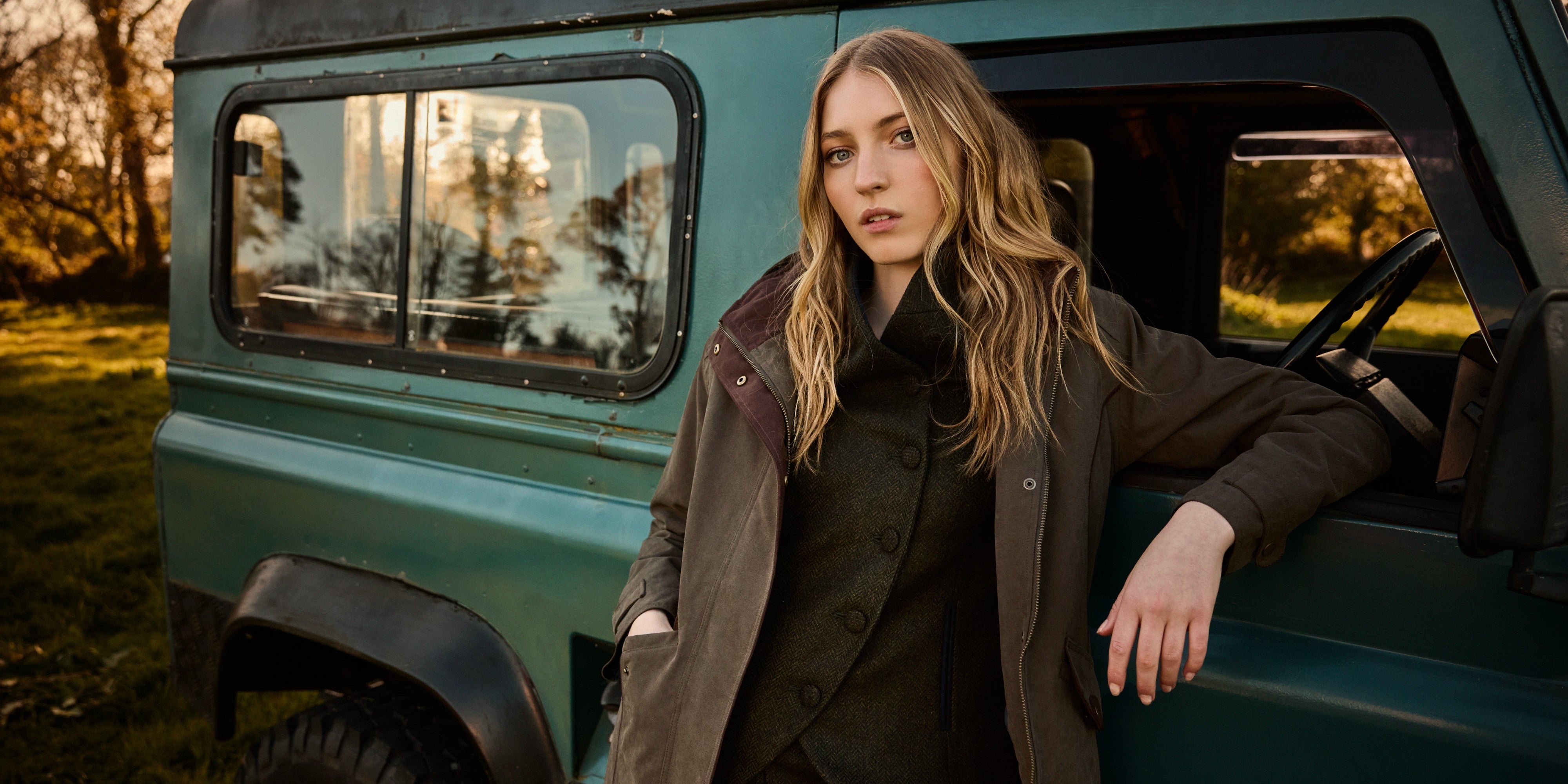 Woman leaning against a vintage green vehicle in a breathable waterproof coat