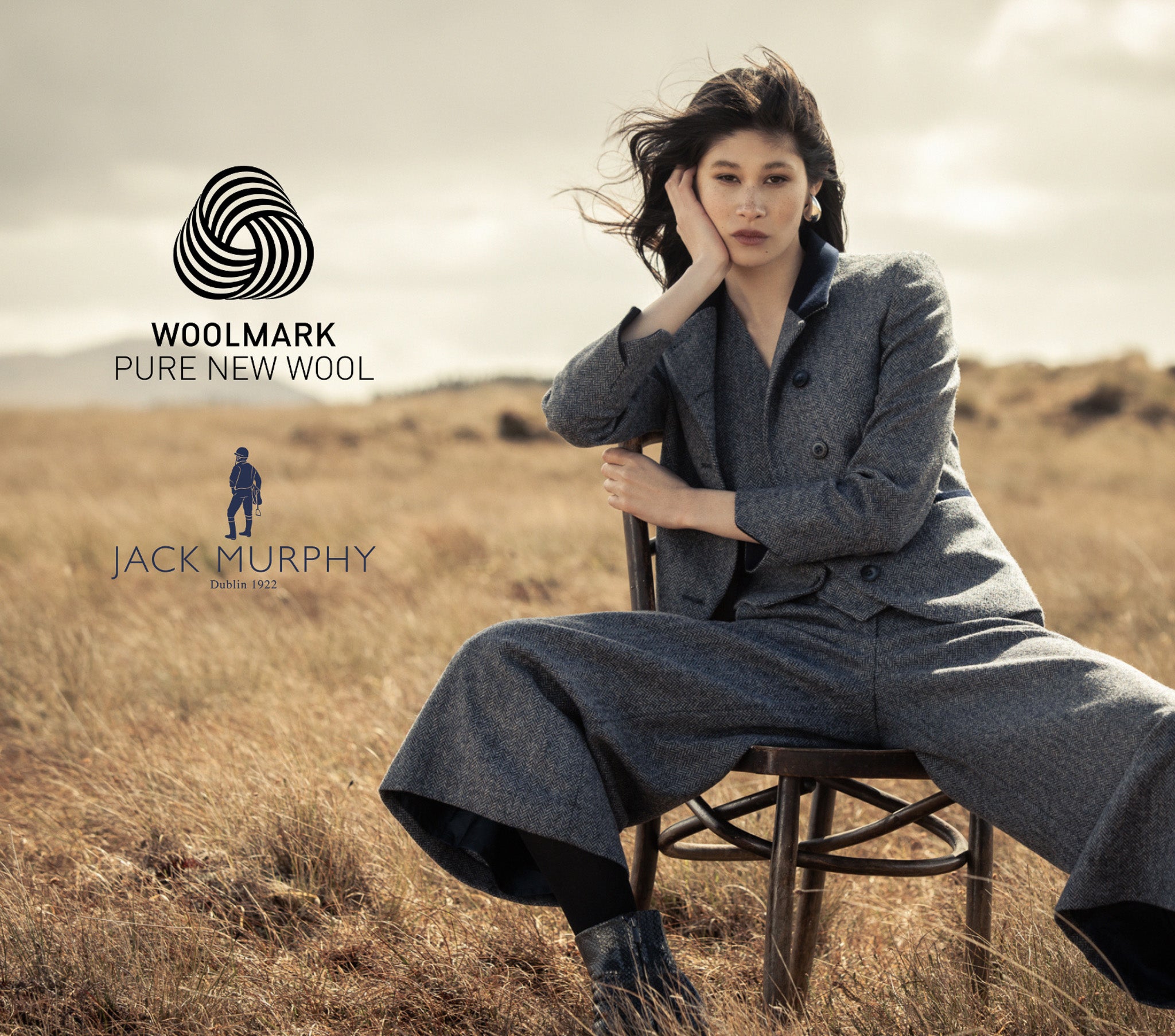  Women in a Jack Murphy three-piece Woolmark-certified merino wool tweed suit sitting in a dune beach landscape.